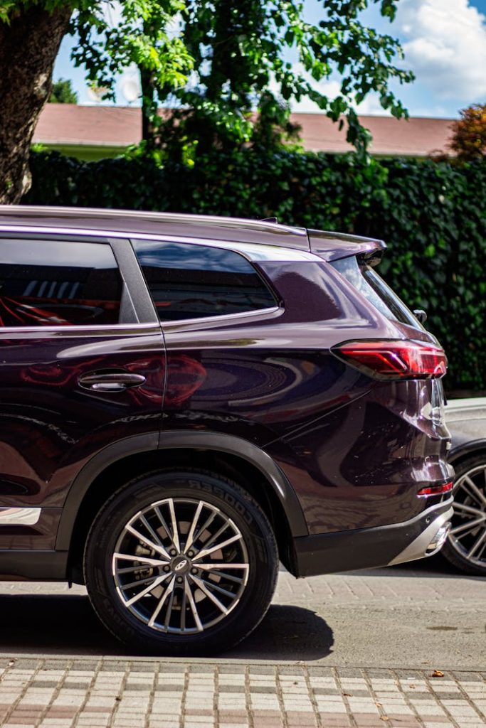 A stylish dark red SUV parked under a tree on a sunny day, showcasing modern design.